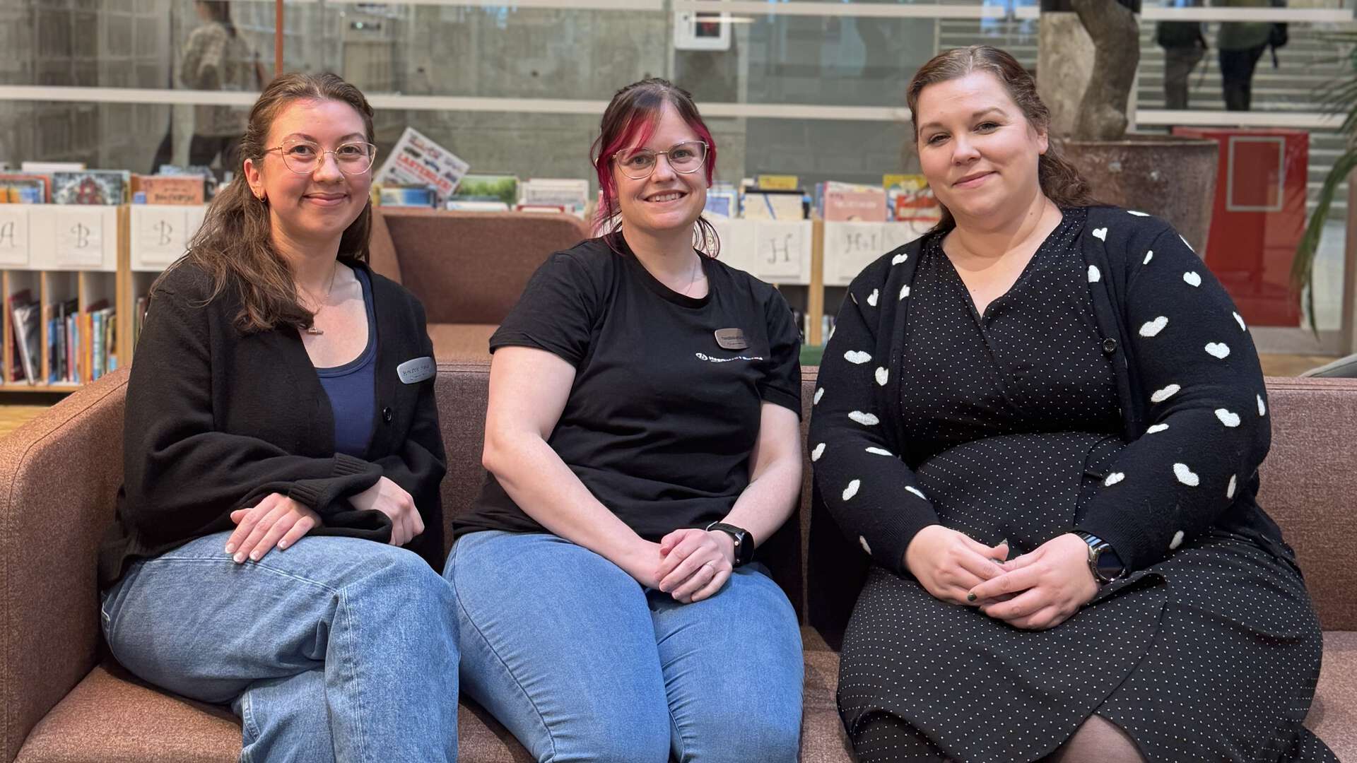 Tre kvinner sitter i en sofa i HiØ-biblioteket og smiler til kamera