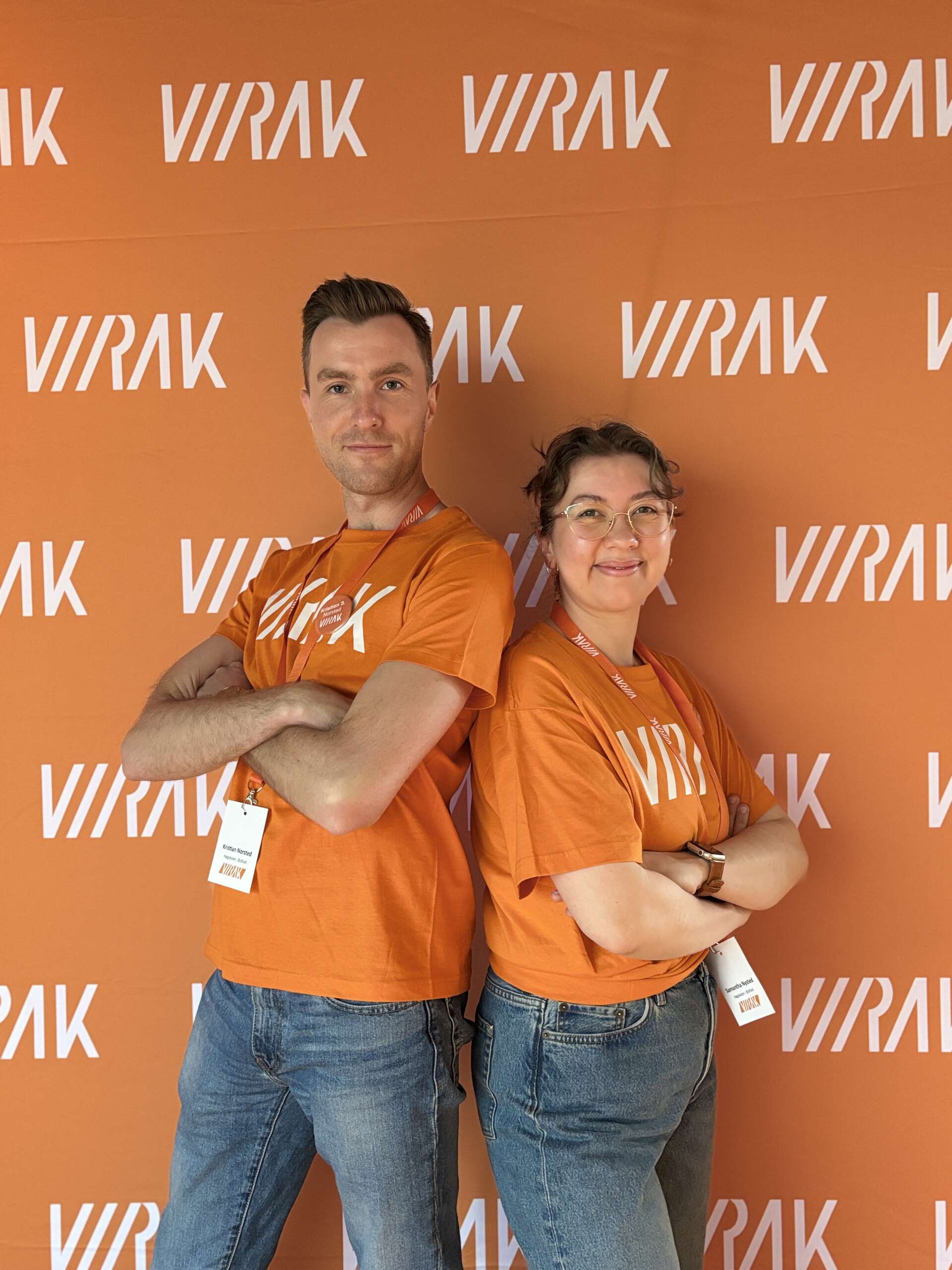 En mann og en kvinne står rygg til rygg foran en VIRAK-fotovegg