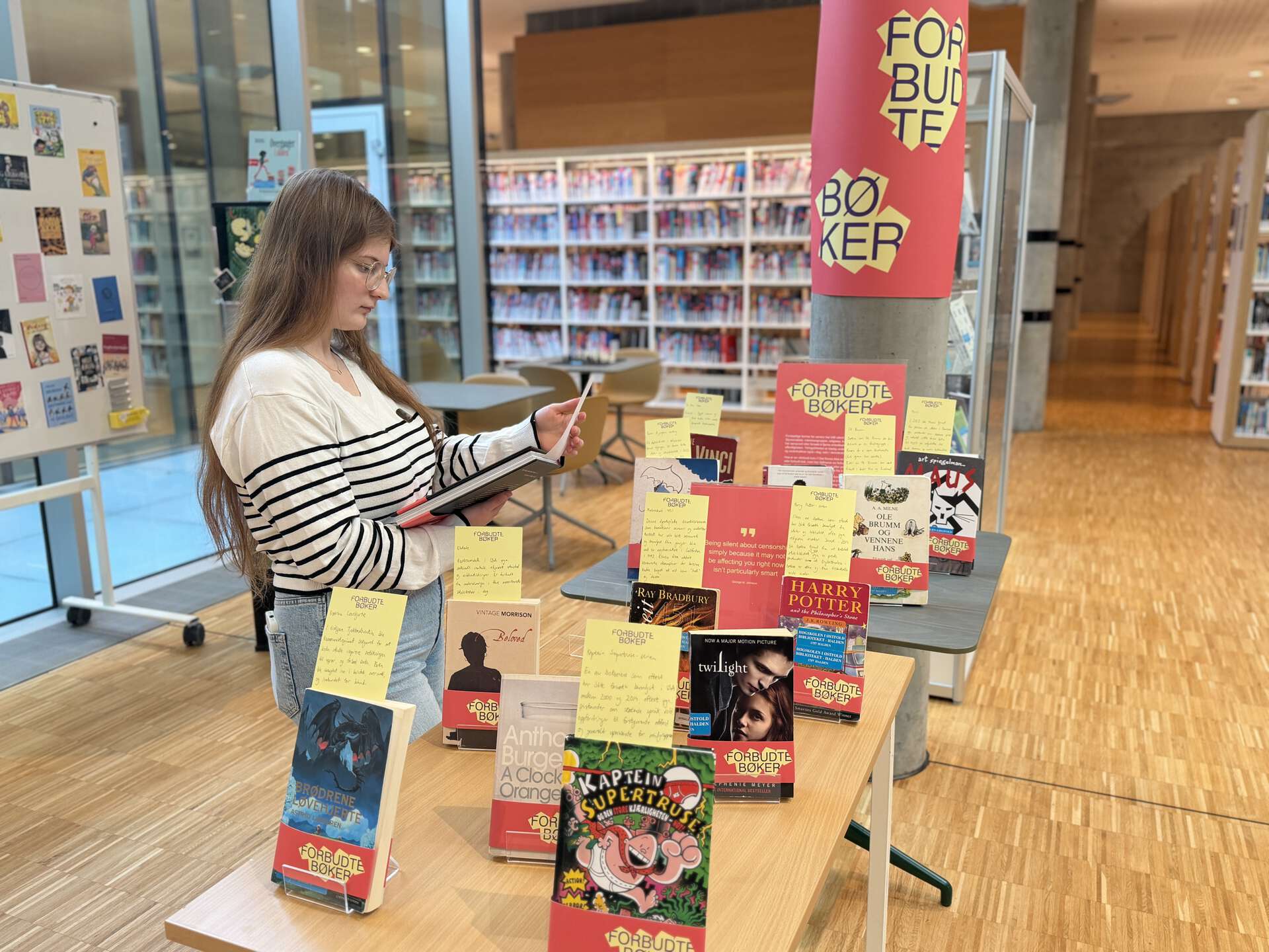 En kvinne står ved en utstilling om forbudte bøker og holder en bok i hendene som hun ser på.
