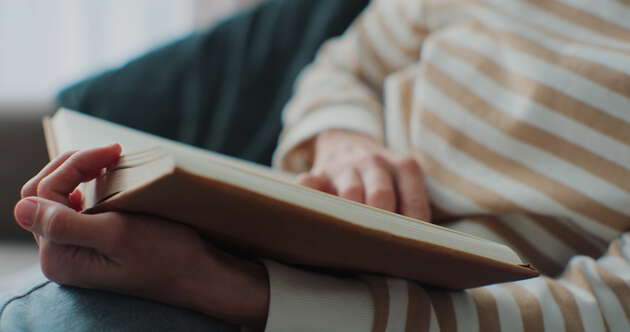 En person sitter ved et bord og leser i en bok