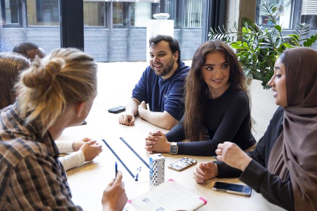 Students gathered around a table, engaged in conversation. Photo. 