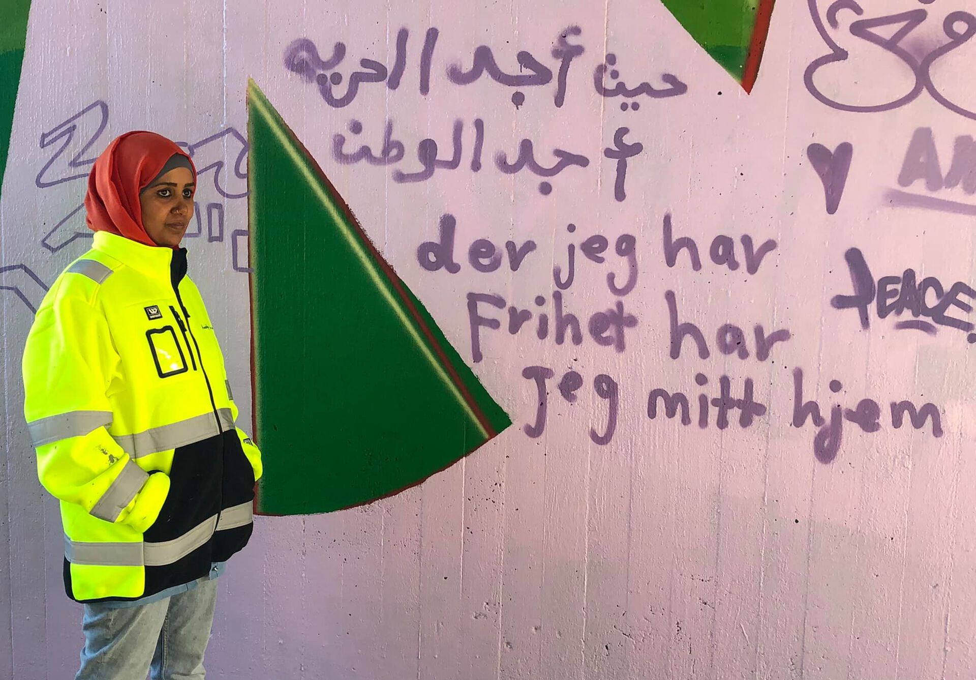 Bildet viser en av flyktningene som deltok i prosjektet foran budskapet hun skrev på veggen. 