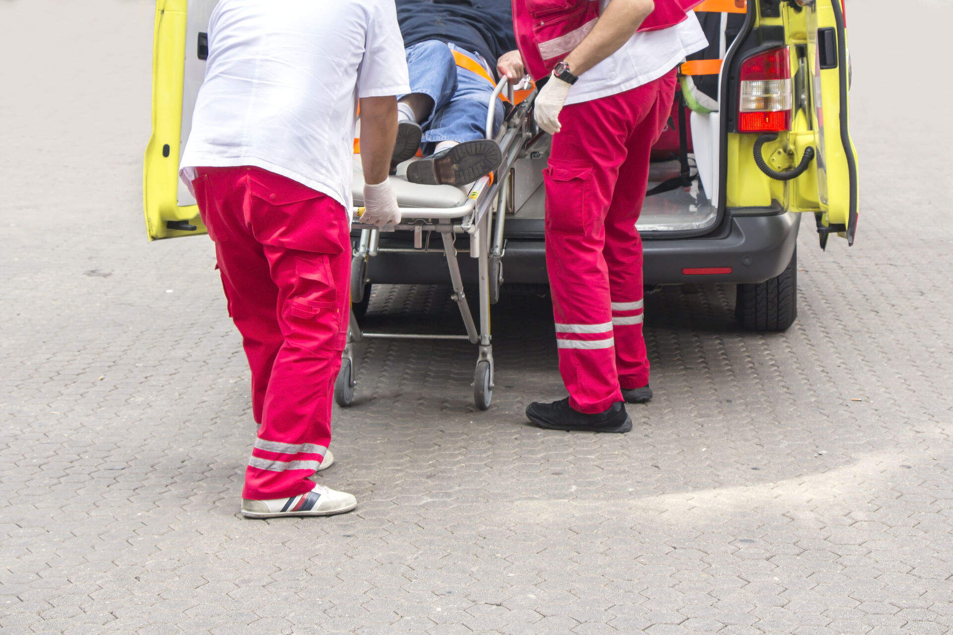 Bildet viser nedre et utsnitt av bakdøren på en ambulanse samt beina til to  ambulansearbeidere som triller en pasient inn i bilen. 