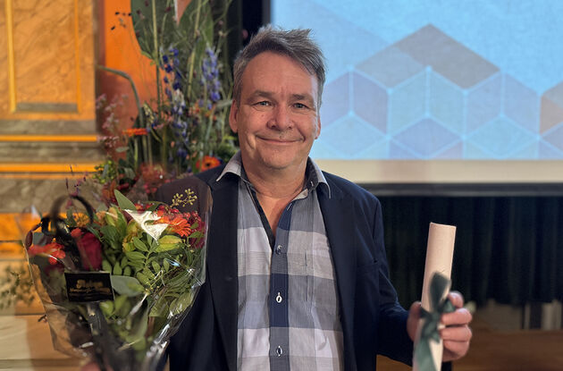 Bildet viser en smilende prisvinner med blomst og diplom. 