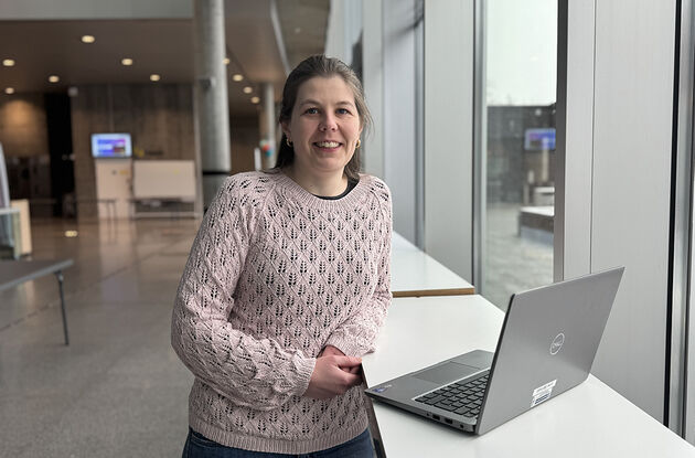 Bilde viser forskeren avbildet foran en pc i et fellesområde på høgskolens campus.