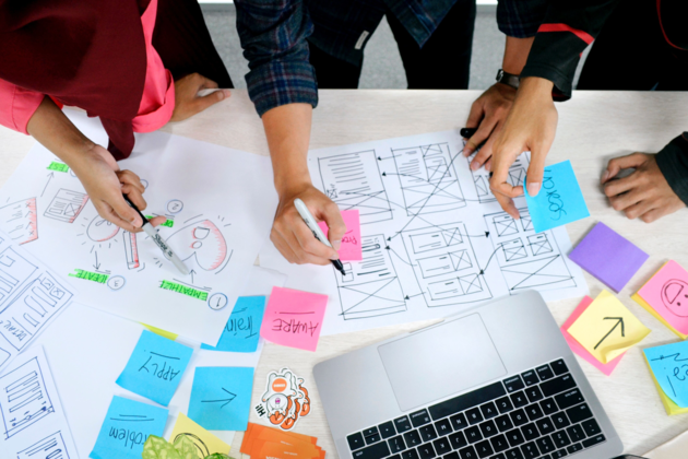 Mennesker som jobber sammen om Design Thinking ved å skrive på Post-its og tekst skisser.