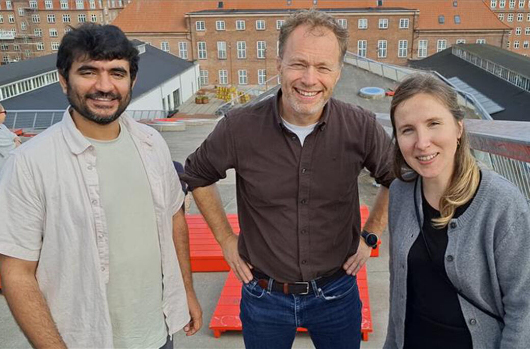Bildet viser de tre forskerne på taket av en stor bygning og med et annet bygg i bakgrunnen. 