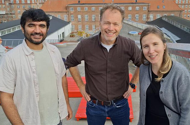 Bildet viser de tre forskerne på taket av en stor bygning og med et annet bygg i bakgrunnen. 