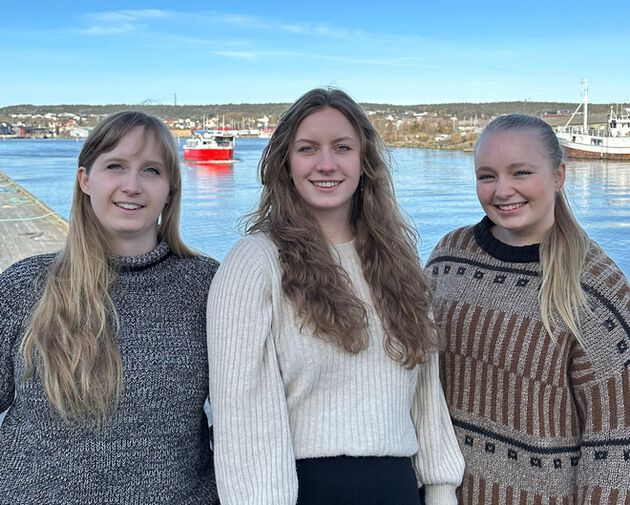 De tre prosjektmedlemmene står på bryggekanten med byfergen i Fredrikstad i bakgrunnen.