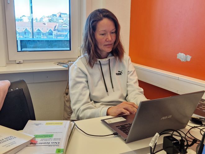 Studenten sitter på et rom på høgskolen og jobber foran en laptop.