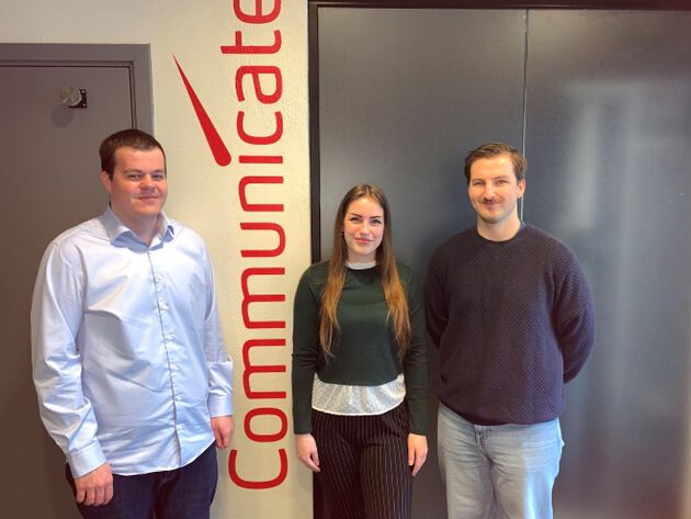 De tre prosjektdeltakerne Kristian Nygård, Ida Tveiterås og Kjell Mikael Karlsen står på rekke foran en vegg med teksten "Communicate".