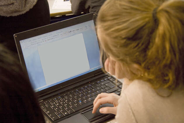Bildet viser et barn som sitter foran en pc-skjerm og ser ned på tastaturet. 