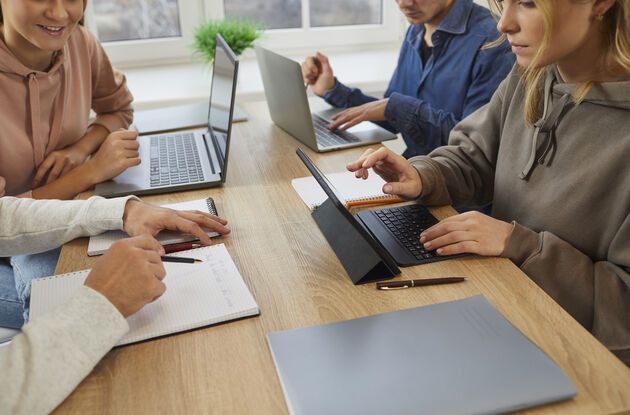 Bildet viser elever som sitter rundt et bord og jobber sammen på pc og nettbrett. 