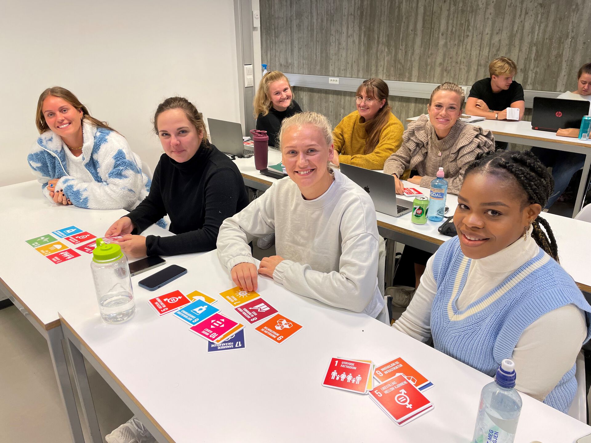 I forgrunnen av bildet sitter 4 kvinnelige studenter ved Grunnskolelærerutdanningen og arbeider med sitt Entreprenørskapsprosjekt. Flere studenter ses i bakgrunnen.