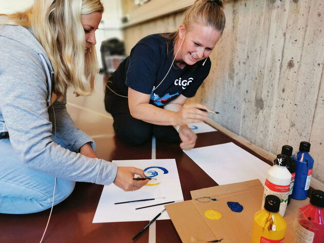 Bildet viser to deltakere på workshop som sitter på gulvet og maler. 