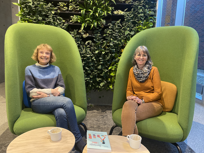 Bilde av forskerne Marianne Maugesten og Kari Spernes på campus i Halden med boken på bordet foran seg. 
