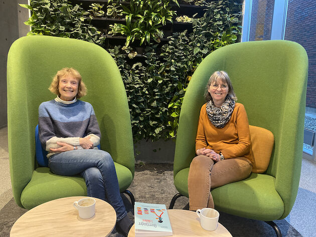 Bilde av forskerne Marianne Maugesten og Kari Spernes på campus i Halden med boken på bordet foran seg. 