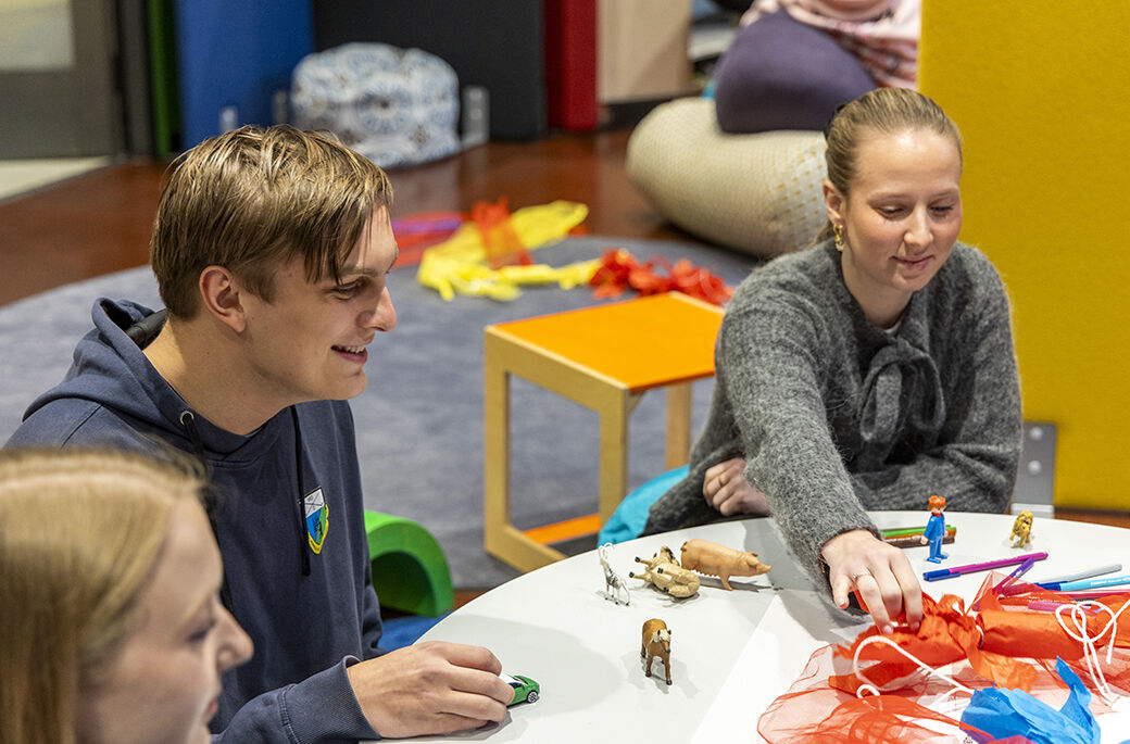 Bildet viser studenter i  samtale og lek rundt et bord. 