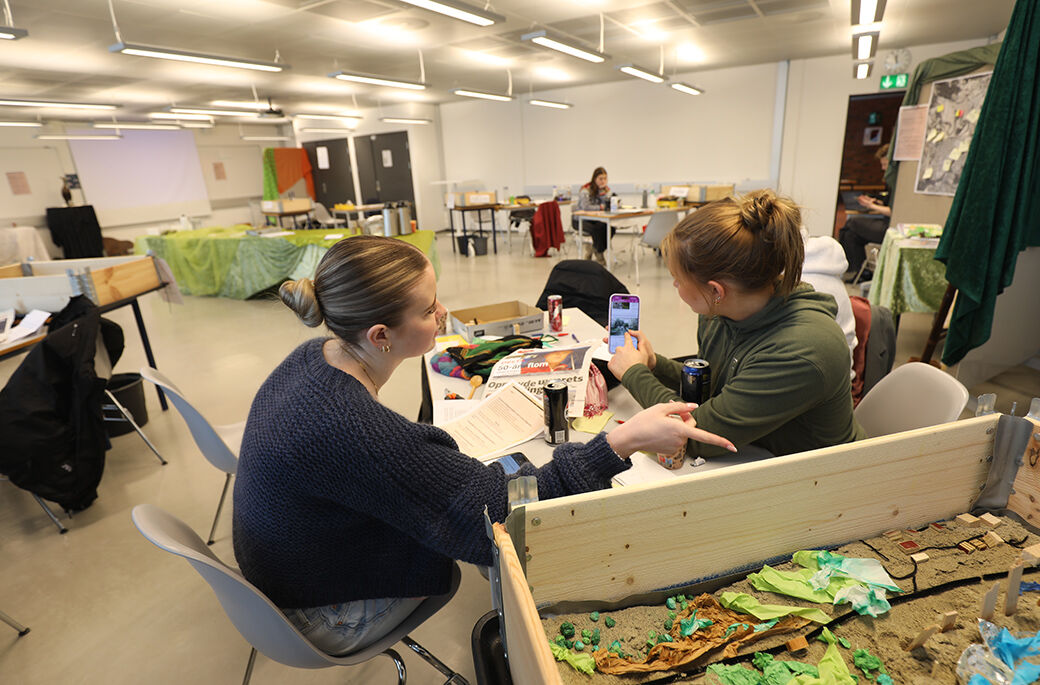 Bildet viser to studenter i kreativ samtale ved en pallekasse der de har bygget en modell av et mikrosamfunn. 