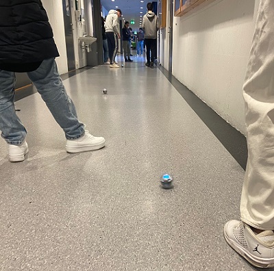 Studentar og elevar er i ein gong og følgjer med på kuler som flyttar seg på golvet.