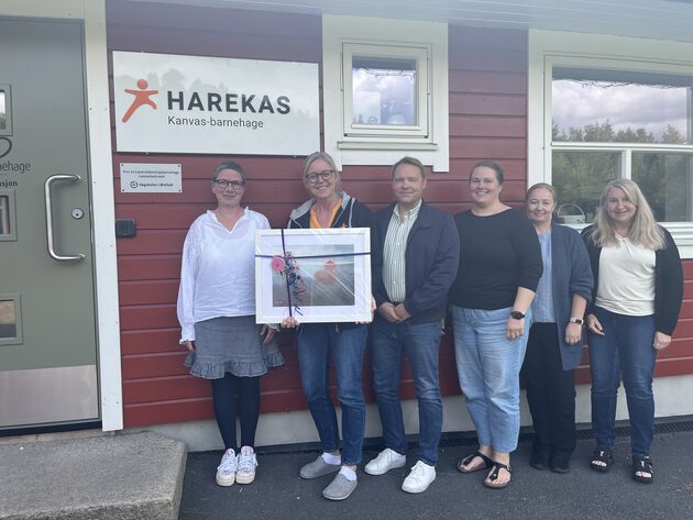 Styringsgruppen i LUB står ved inngangspartiet til Harekas barnehage. Tone Ingvaldsen, styrer i barnehagen, holder i et bilde som er gave og gratulasjon til barnehagen fra LUB. 