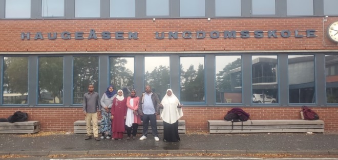 Studentene fra Zanzibar står utenfor Haugeåsen ungdomsskole. Navnet på skolen står oppført på veggen.