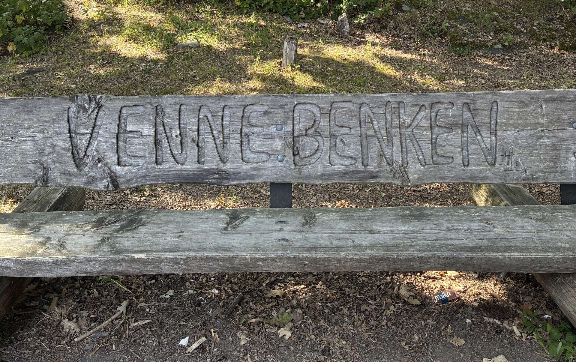 Utendørs benk med "Vennebenken" innrisset i ryggen.