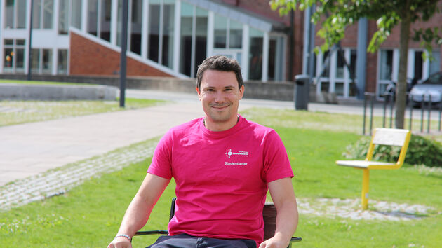 Studentleder Martin Arthur Andersen avbildet på en stol foran hovedbygningen på campus  i Fredrikstad. 
