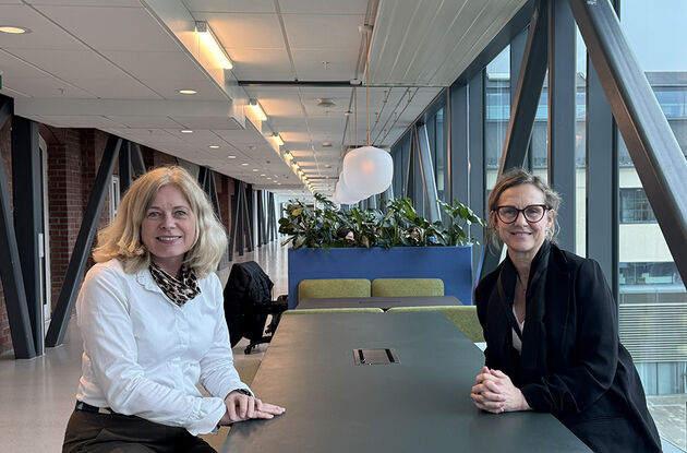 Bildet viser høgskolens nye Site Director  og prodekan for utdanning sittende  ved et langt bord i et av høgskolens fellesarealer. 