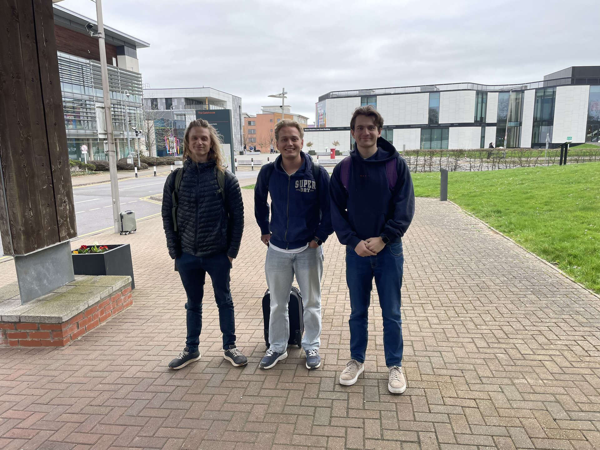 Tre av studentene avbildet sammen utendørs foran campusbygninger i England.