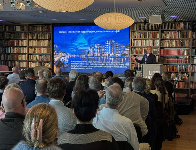 Bildet viser HiØ-rektoren som holder en presentasjon foran en fullsatt sal og med et bilde av bysentrum på storskjerm i bakgrunnen.  