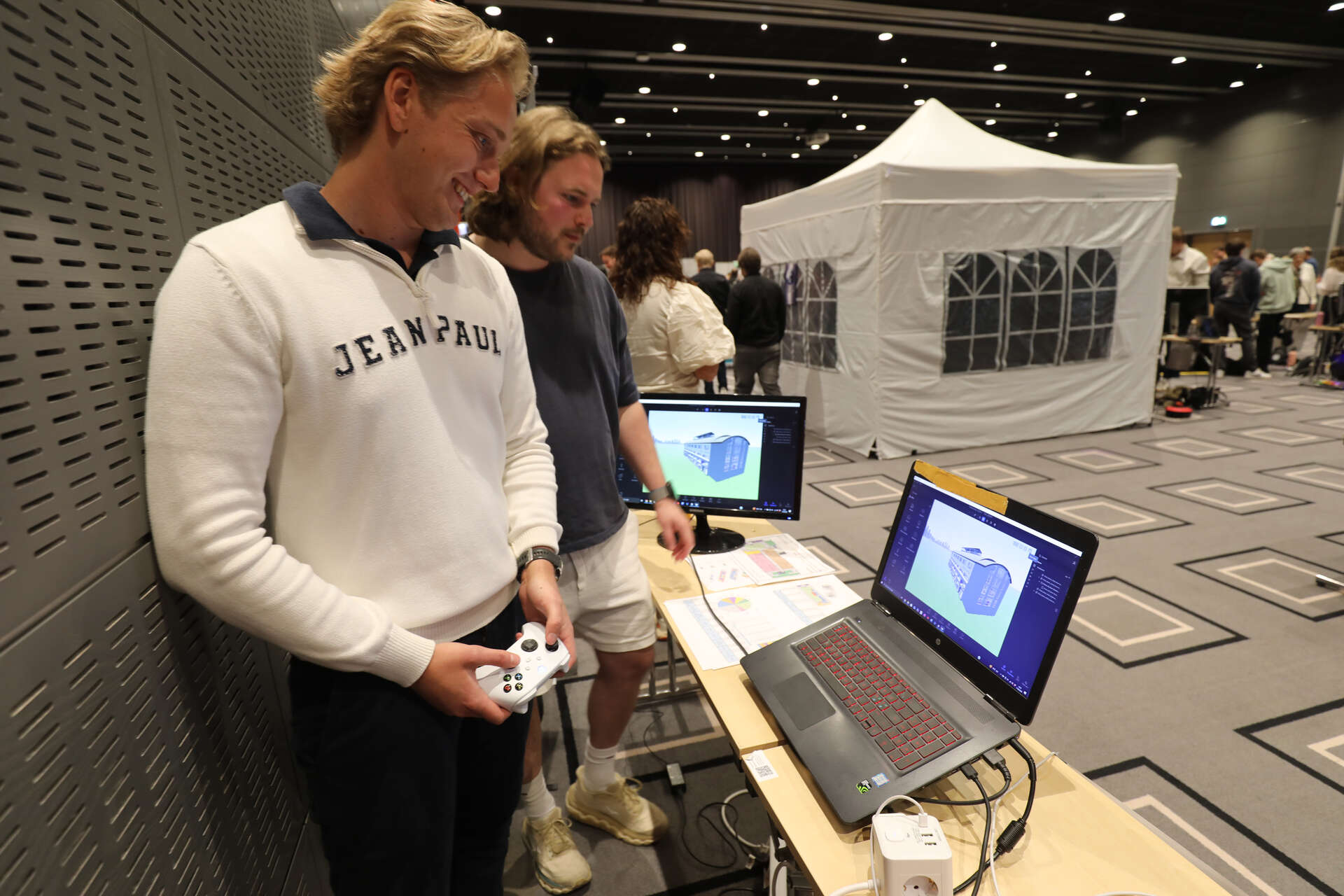 To av bachelorstudentene står foran en pc-skjerm og demonstrerer modellene de har laget.