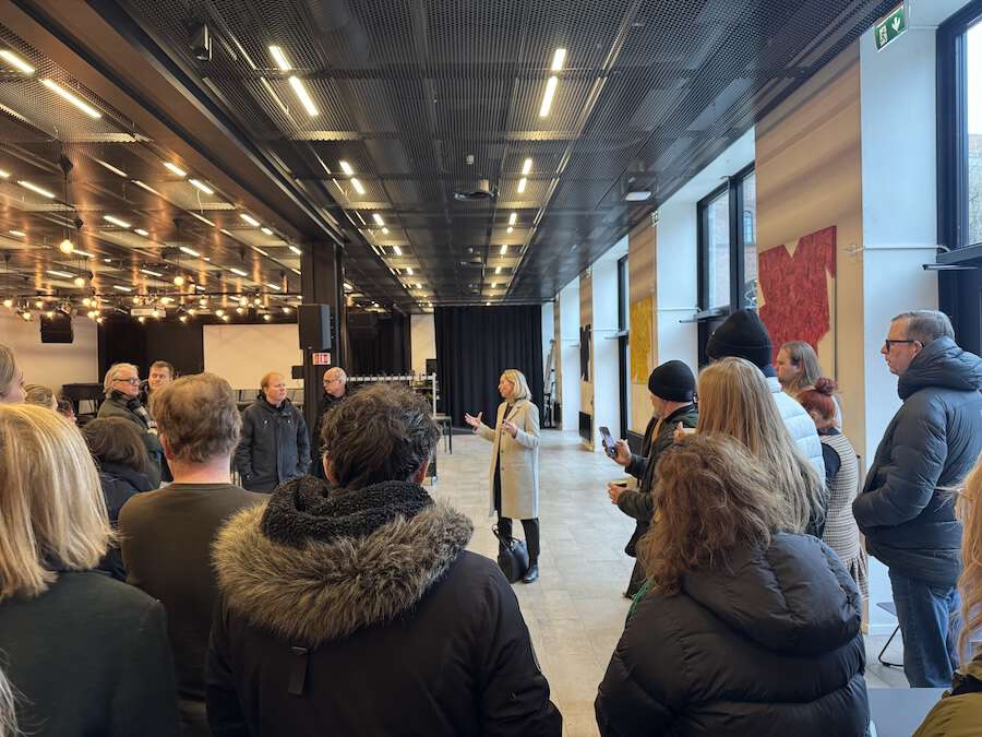 Bildet viser en gruppe mennesker i et stort rom som lytter til informasjon fra en person som står plassert i senter av bildet. 