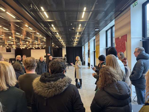 Bildet viser en gruppe mennesker i et stort rom som lytter til informasjon fra en person som står plassert i senter av bildet. 