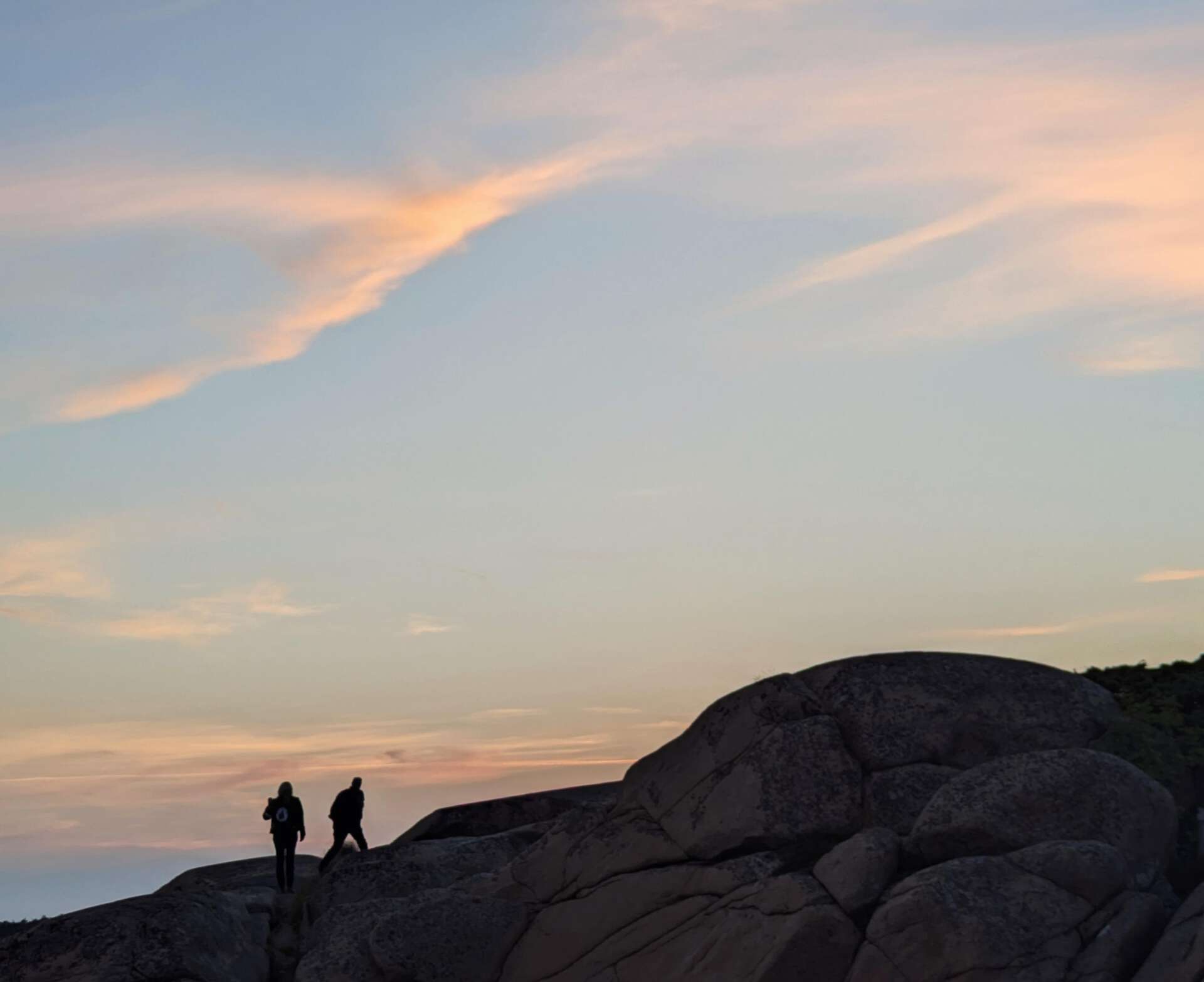 Silhuetter av to personer som går på et fjell i solnedgang.