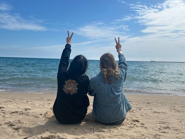 to jenter sittende på strand med ryggen til blå himmel og peace tegn